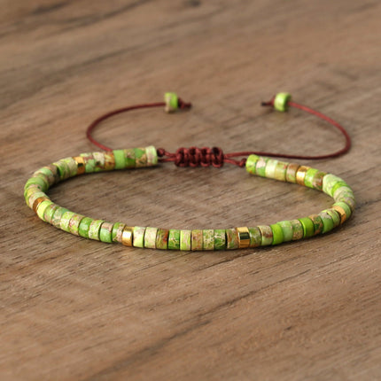 Natural stone beaded adjustable bracelet featuring green and gold spacer beads on a wooden background.