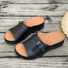 Black sandals with tan soles on a wooden surface