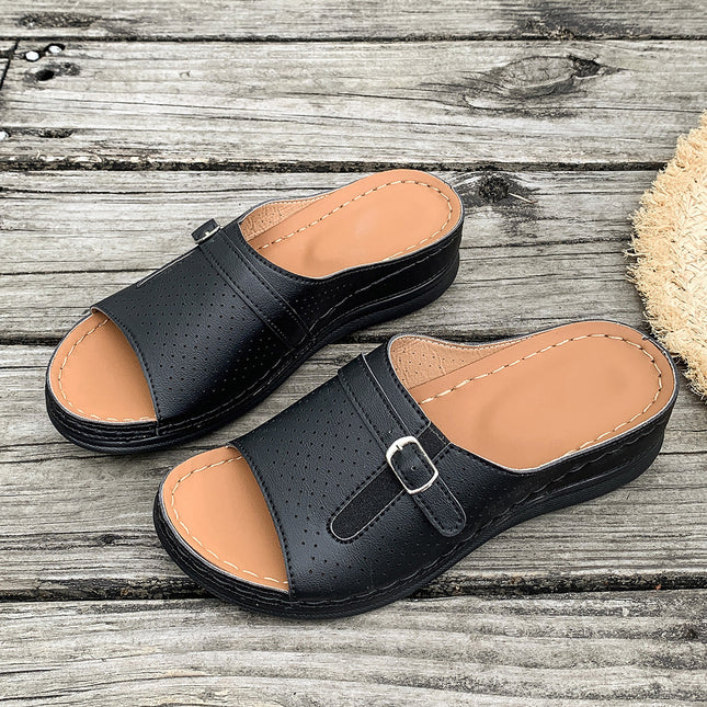 Black sandals with tan soles on a wooden surface