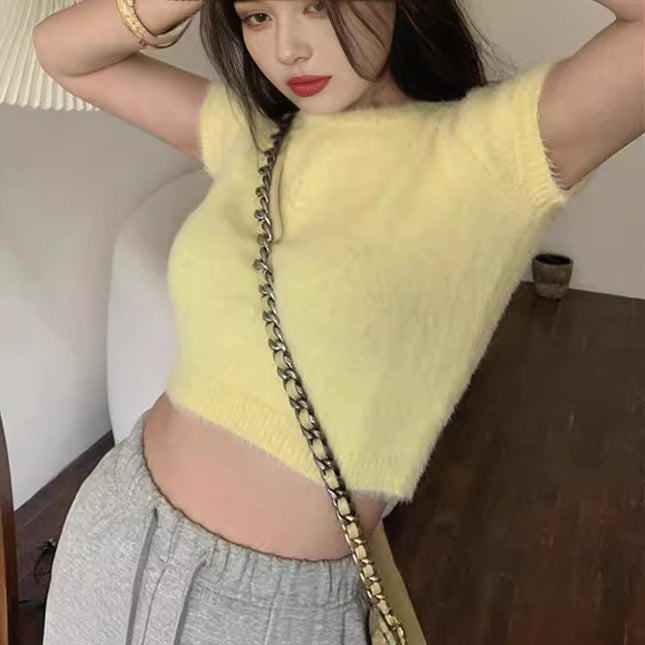 Person wearing a yellow sleeveless top and gray pants, holding a beige handbag with a chain strap.