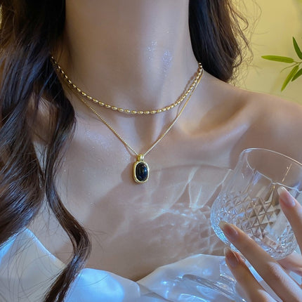 Woman wearing a gold necklace with a black pendant, holding a clear glass.