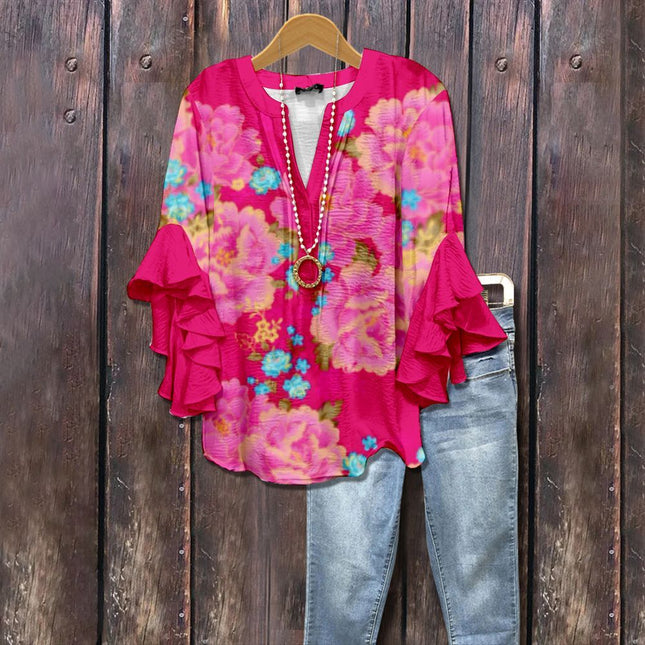Pink floral blouse with ruffled sleeves on a hanger against a wooden background