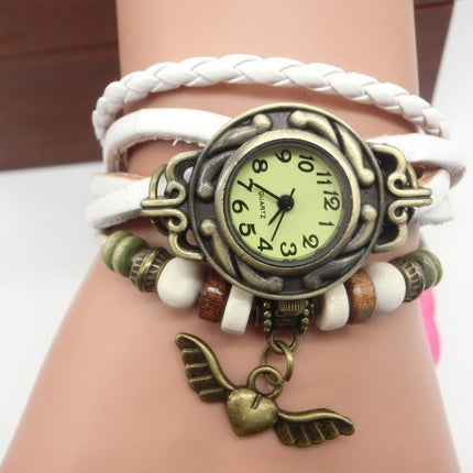 Wrist wearing a decorative watch with a white braided strap and wing charm on a plain background