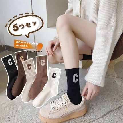 Person wearing black socks with a letter 'C' design, surrounded by five pairs of similar socks.