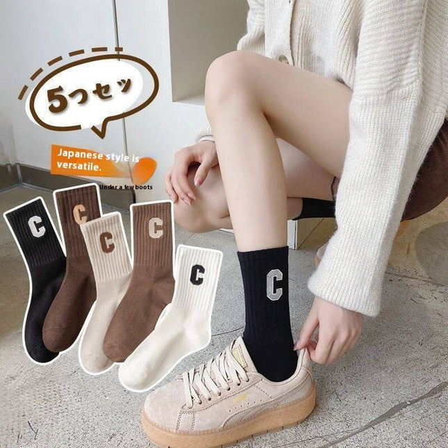 Person wearing black socks with a letter 'C' design, surrounded by five pairs of similar socks.