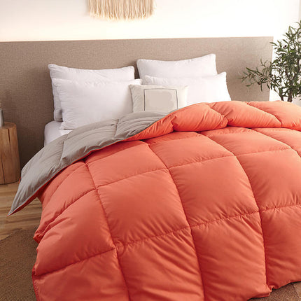 Orange quilt on a bed with white pillows and a plant in the corner.