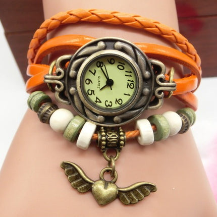 Multicolored braided bracelet with a vintage-style watch face and heart-shaped pendant on a wrist.