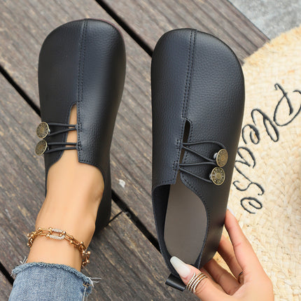 Black loafers with decorative buttons on a wooden floor