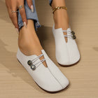 White loafers with decorative buttons worn by a person on a wooden floor.