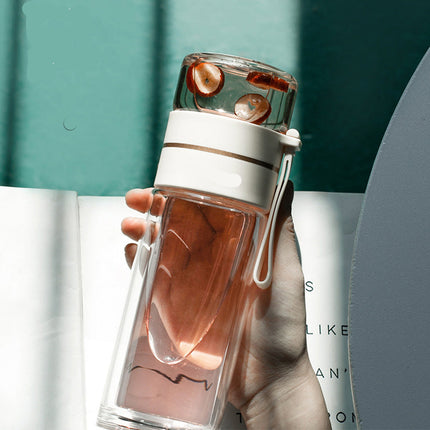 Clear glass water bottle with white base held by a hand against a blurred background