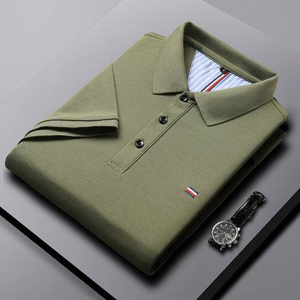 Folded green polo shirt with a brand logo on a gray surface, next to a watch.