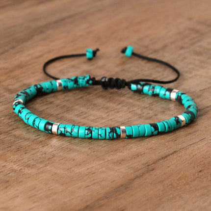 Turquoise beaded bracelet with black cord on a wooden surface