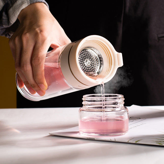 Hand pouring pink liquid from a small container into a glass jar on a table.