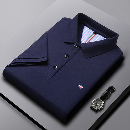 Folded navy blue polo shirt with a brand logo on a gray surface, accompanied by a black watch.