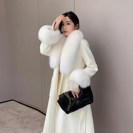 Woman wearing a white coat with fur trim holding a black handbag against a neutral background