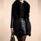 Person wearing a black coat with fur collar and leather skirt on a beige background