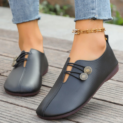 Black loafers with decorative buttons worn by a person on a wooden floor.