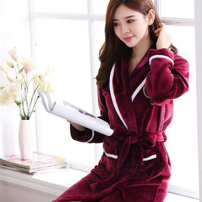 Woman in a burgundy robe holding a book in a bright room with flowers and books on a surface.