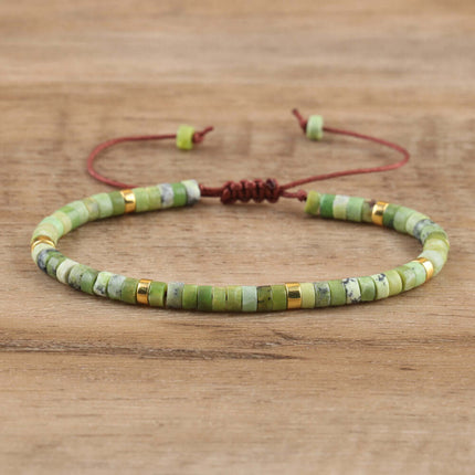 Adjustable women's bracelet with green natural stone beads and decorative gold spacers on a wooden background.
