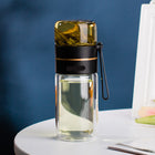 Clear glass bottle with black lid and handle on a white surface with a blue background