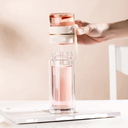 Hand holding a glass water bottle with a pink liquid on a white surface.