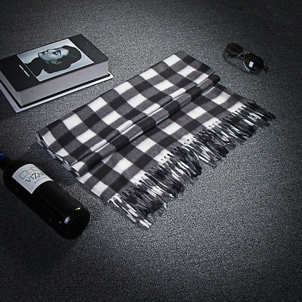 Black and white checkered scarf with tassels on a dark surface, next to a bottle and sunglasses.