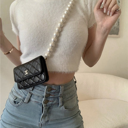 Person wearing a white cropped sweater, blue jeans, and carrying a black Chanel handbag with a pearl strap.