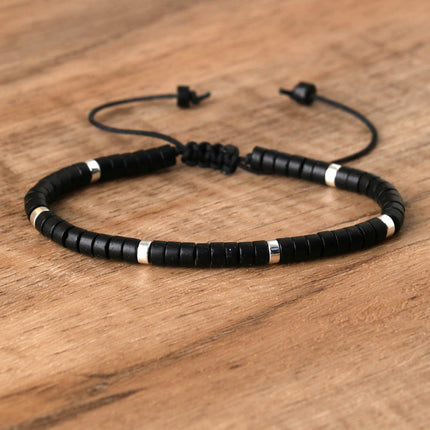Black adjustable beaded bracelet with silver accents on wooden background.