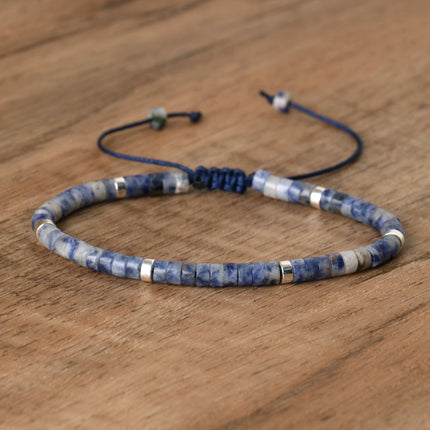 Hand-woven adjustable spacer bead bracelet featuring blue and silver stones on a wooden surface.