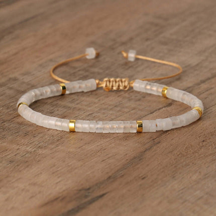 Adjustable beaded bracelet with clear stones and gold accents on wooden background.