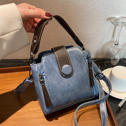 Blue handbag with a strap held by a hand on a wooden surface.