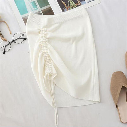 White knitted high waist skirt with ruched design and drawstrings, styled with glasses and sandals on a table.