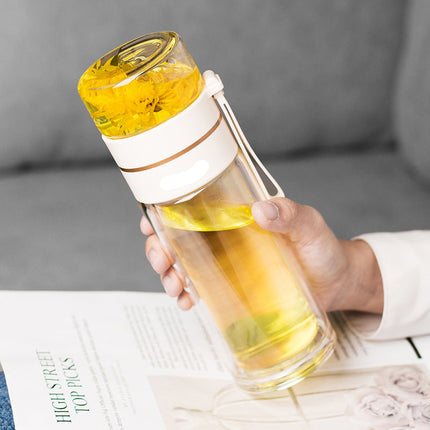 Hand holding a transparent water bottle with yellow liquid and a white lid, on a gray surface.