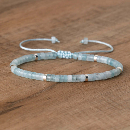 Adjustable beaded bracelet made with natural stone beads in soft blue and metallic accents on wooden surface.