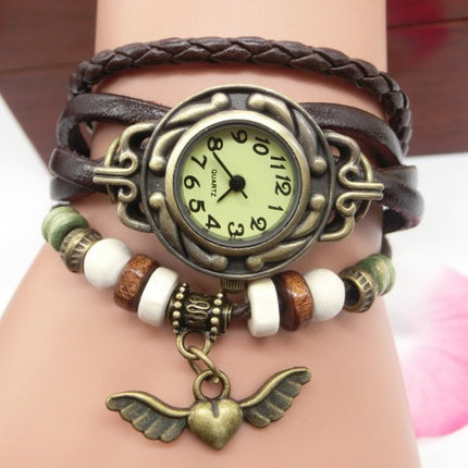Bracelet with vintage-style watch and heart pendant on wrist against a neutral background
