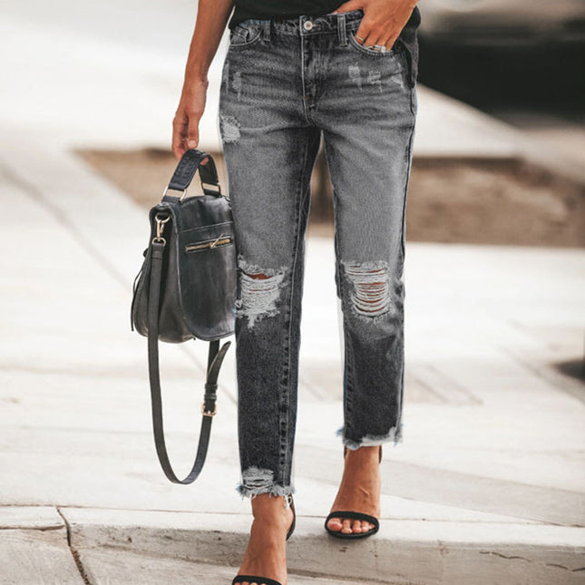 Person wearing distressed gray jeans with a black handbag on a blurred background