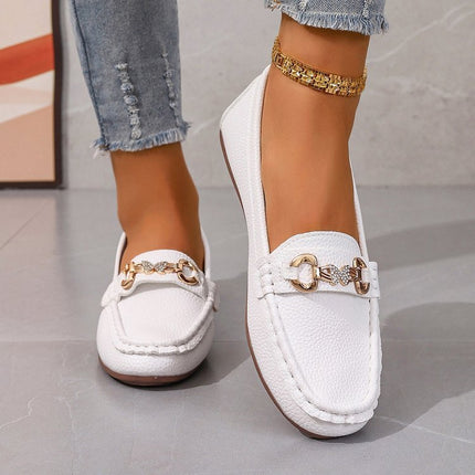 White loafers with gold buckles worn by a person on a neutral background