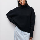 Person wearing a black sweater and light blue jeans against a white background