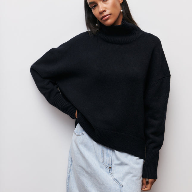 Person wearing a black sweater and light blue jeans against a white background