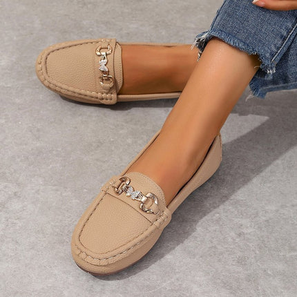Beige loafers with decorative chain detail worn by a person on a gray surface