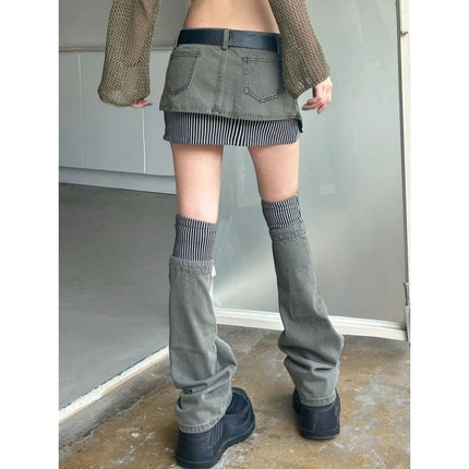 Person wearing a green skirt, brown cardigan, and gray high-waisted pants with black shoes indoors.