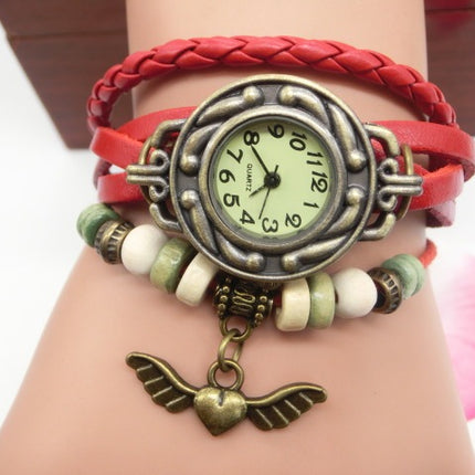 Bracelet with vintage-style watch face and wing charm on a wrist against a white background