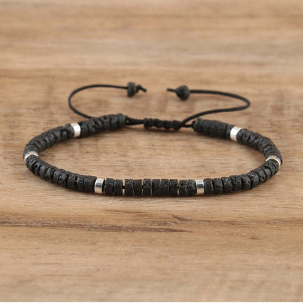 Adjustable black lava stone bracelet with silver accents on a wooden surface.