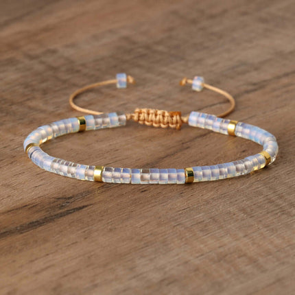Hand-woven adjustable bracelet with iridescent beads and gold accents on a wooden surface.