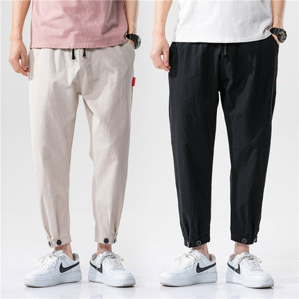 Two people wearing beige and black pants with white sneakers on a plain background