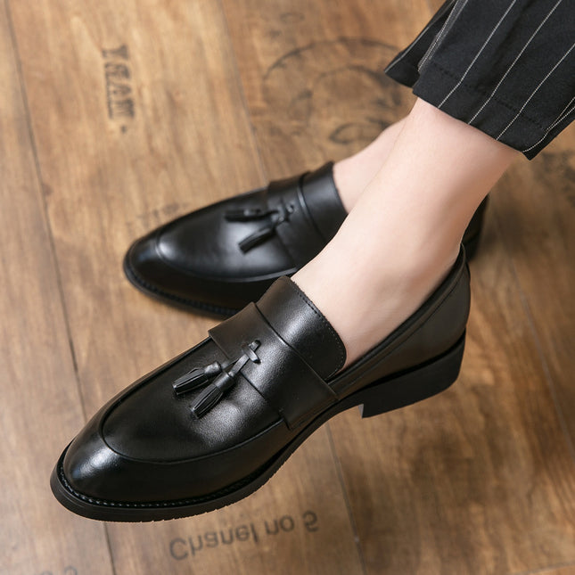 Black leather loafers with tassels worn on a wooden floor