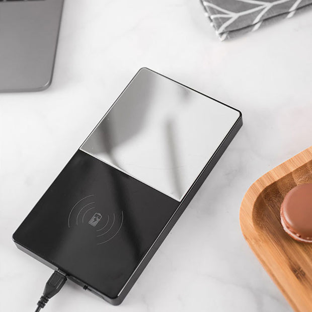 Wireless charging pad on a white surface with a wooden coaster and remote control in the background.