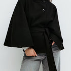 Person wearing a black cape over a plain background
