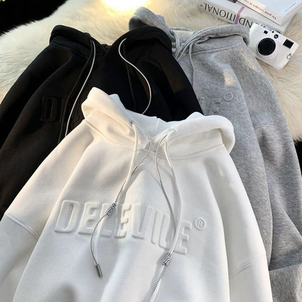 White hoodie with 'DEFEATE' branding on a surface with other clothing items.