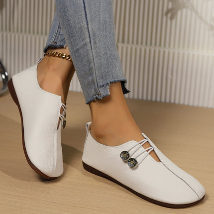 White loafers with brown soles worn by a person on a wooden floor.